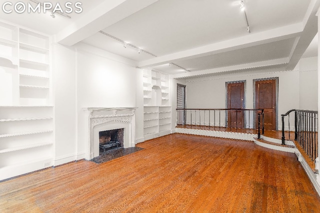 unfurnished living room with hardwood / wood-style flooring, track lighting, built in features, and beamed ceiling