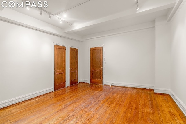 spare room featuring hardwood / wood-style floors, rail lighting, and beamed ceiling