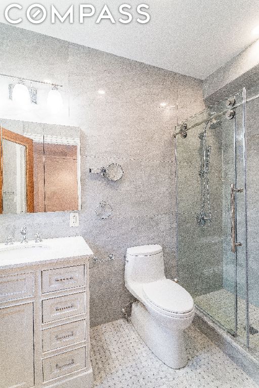 bathroom with vanity, toilet, an enclosed shower, and tile walls