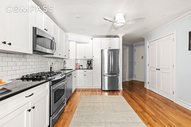 kitchen featuring sink, white cabinetry, light wood-type flooring, appliances with stainless steel finishes, and decorative backsplash