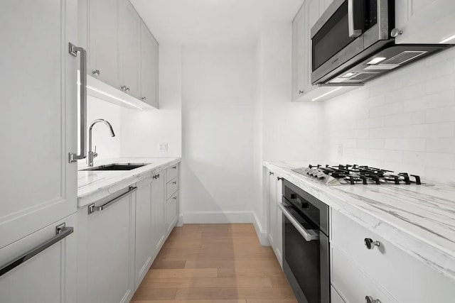 kitchen with white cabinetry, sink, light hardwood / wood-style floors, stainless steel appliances, and light stone countertops