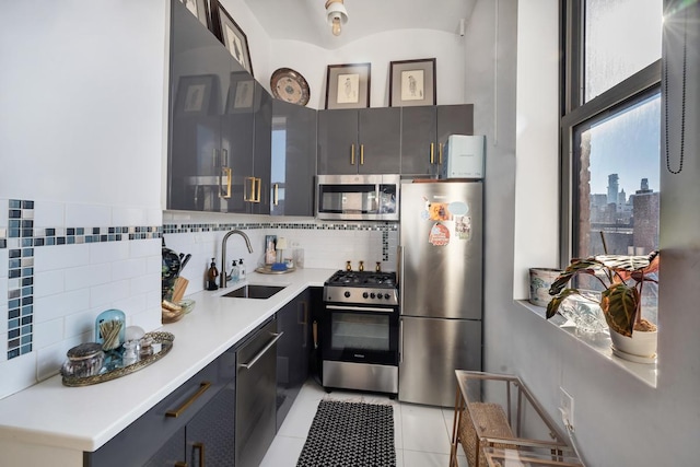 kitchen with light tile patterned floors, light countertops, decorative backsplash, appliances with stainless steel finishes, and a sink