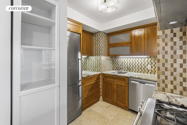 kitchen with tasteful backsplash, light stone countertops, appliances with stainless steel finishes, and sink