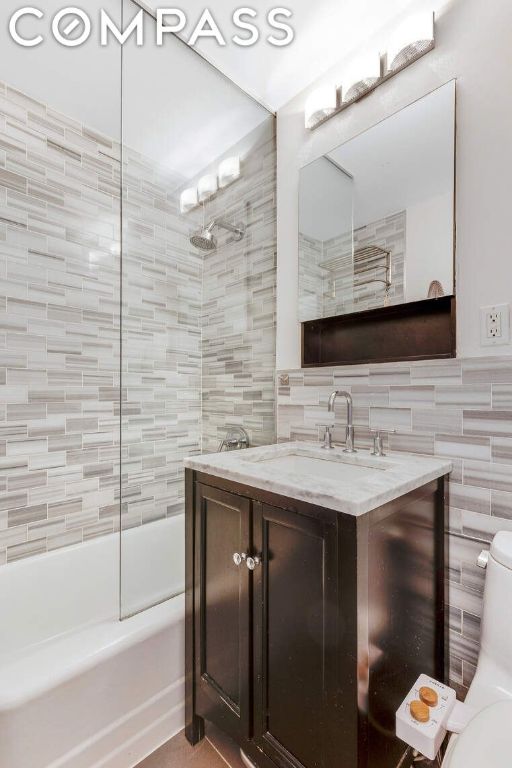 full bathroom with tile walls, tiled shower / bath combo, vanity, tasteful backsplash, and toilet