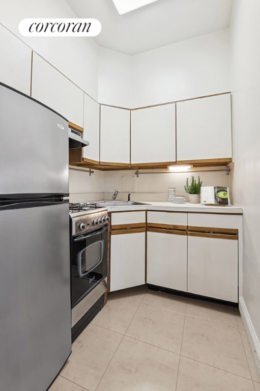 kitchen with light tile patterned floors, range hood, white cabinets, and appliances with stainless steel finishes