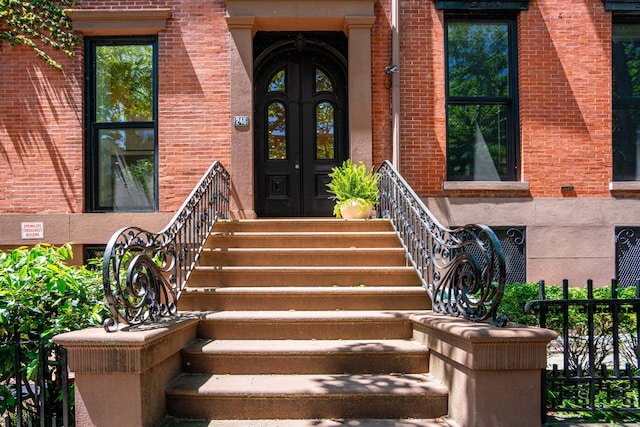 view of exterior entry with brick siding, french doors, and fence