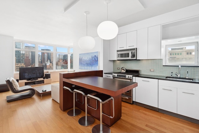 11 E 29th St Unit 27C, New York City, NY 10016 - kitchen featuring stainless steel appliances, dark countertops, light wood-style floors, tasteful backsplash, and white cabinetry