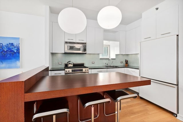 kitchen featuring sink, white cabinetry, pendant lighting, stainless steel appliances, and decorative backsplash