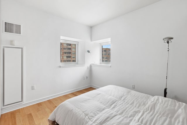 bedroom with baseboards, visible vents, and wood finished floors