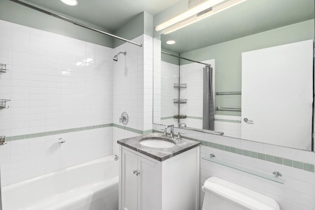 full bathroom featuring tiled shower / bath, vanity, toilet, and tile walls