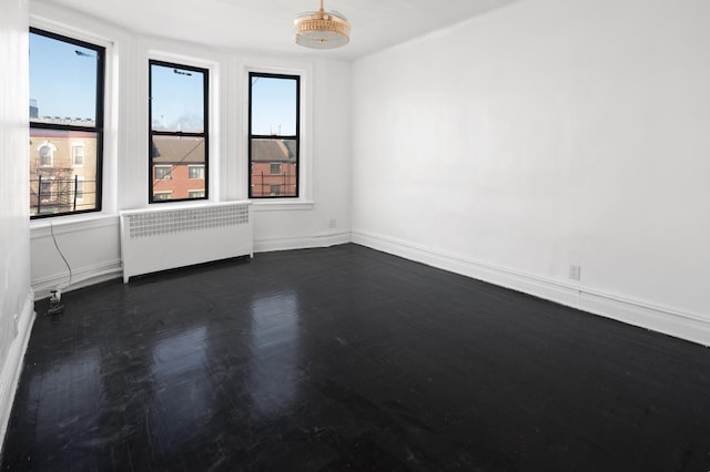 empty room featuring radiator heating unit, baseboards, and dark wood-style flooring