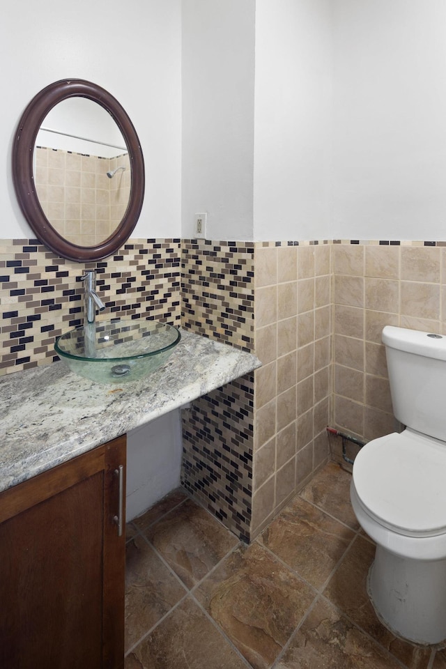 half bath with wainscoting, toilet, tile walls, and a sink