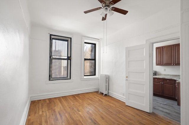 unfurnished room featuring light wood-style flooring, radiator, baseboards, and ceiling fan