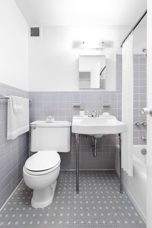 bathroom with visible vents, toilet, tile walls, and shower / tub combo