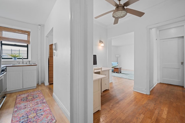 hallway with light wood-type flooring, a sink, baseboards, and crown molding