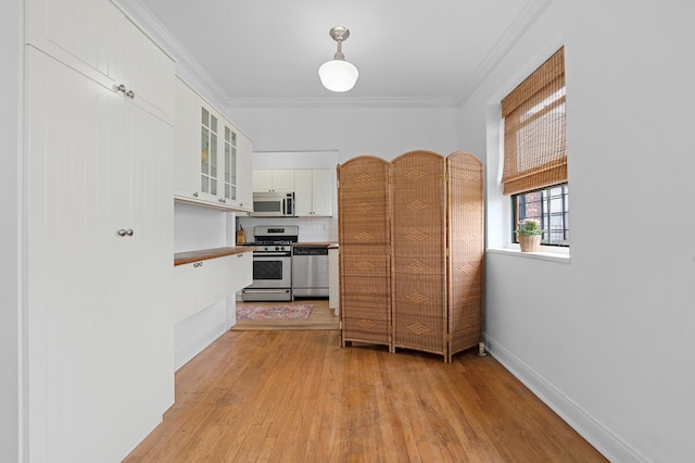 kitchen with appliances with stainless steel finishes, light wood-type flooring, white cabinets, glass insert cabinets, and ornamental molding