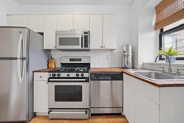 kitchen with stainless steel appliances, butcher block countertops, a sink, white cabinets, and backsplash