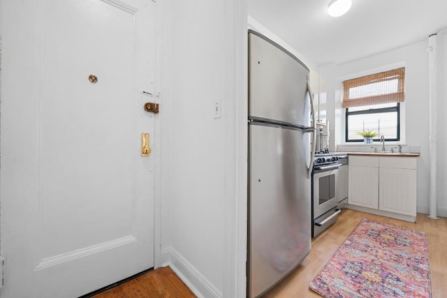 kitchen with light countertops, appliances with stainless steel finishes, a sink, light wood-type flooring, and baseboards