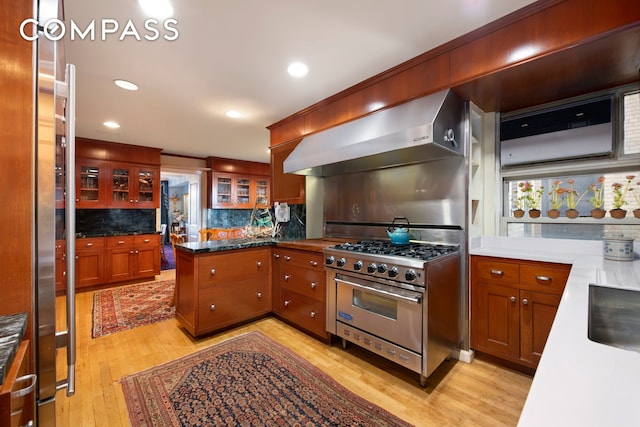 kitchen featuring stainless steel stove, wall chimney exhaust hood, light wood finished floors, decorative backsplash, and recessed lighting