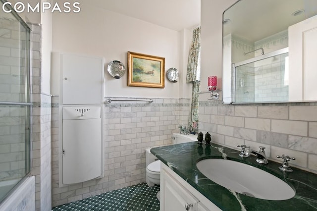 full bathroom featuring shower / bath combination with glass door, vanity, toilet, and tile walls