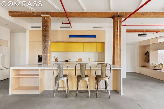 kitchen with beam ceiling, concrete flooring, paneled refrigerator, a kitchen bar, and light brown cabinetry