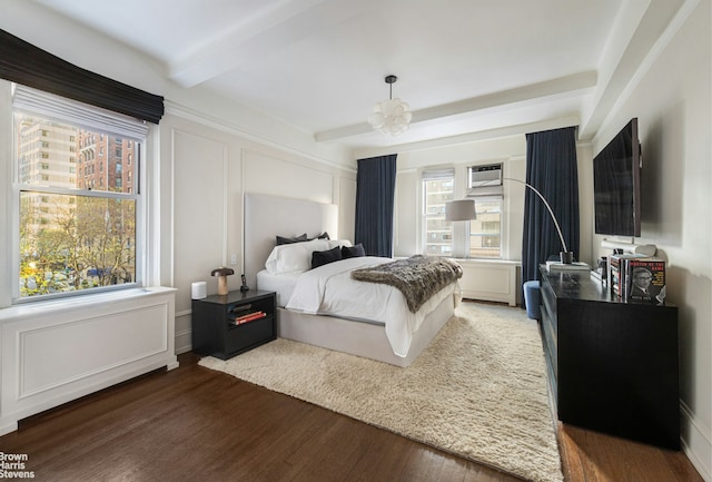 bedroom with beam ceiling, a decorative wall, and wood finished floors