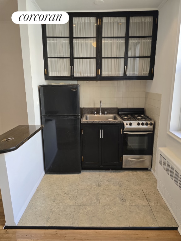 kitchen with black refrigerator, radiator, tasteful backsplash, sink, and stainless steel gas range oven