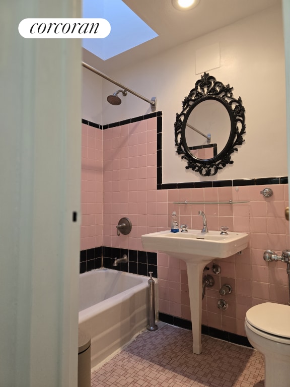 bathroom featuring tiled shower / bath, a skylight, tile walls, tile patterned flooring, and toilet