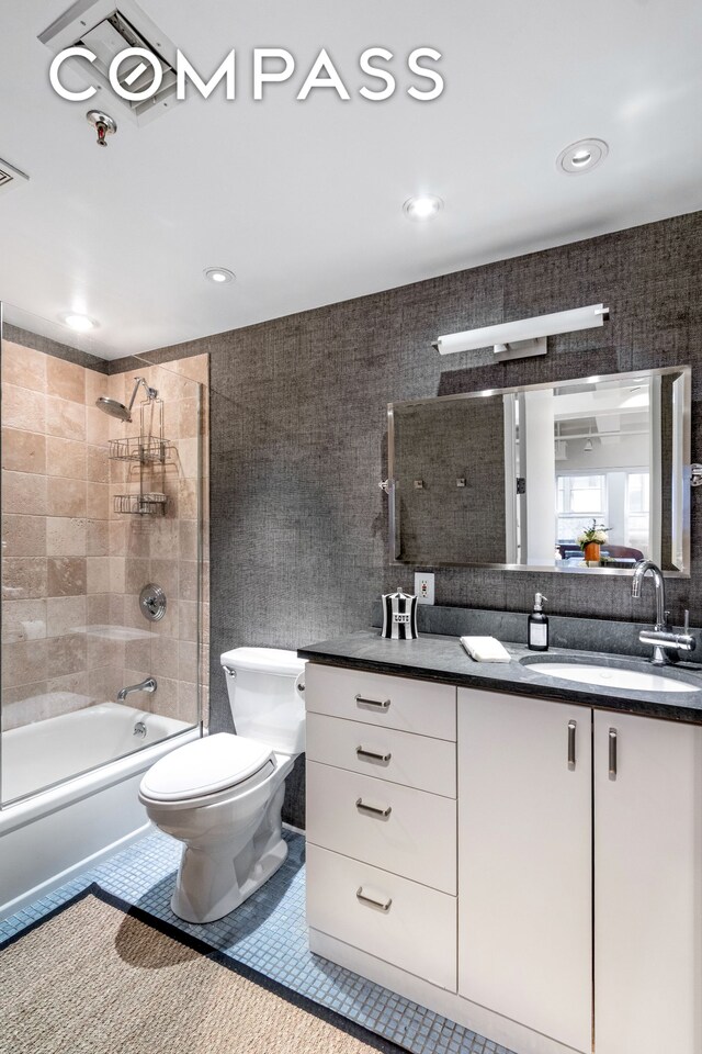 full bathroom featuring tiled shower / bath, tile walls, vanity, and toilet