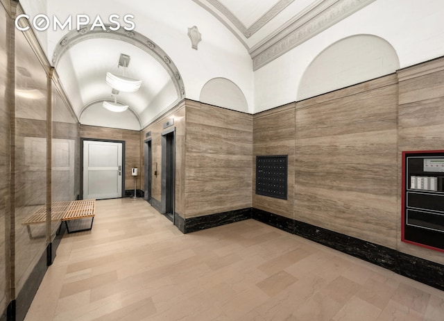 hall featuring mail area, ornamental molding, wood finished floors, elevator, and vaulted ceiling