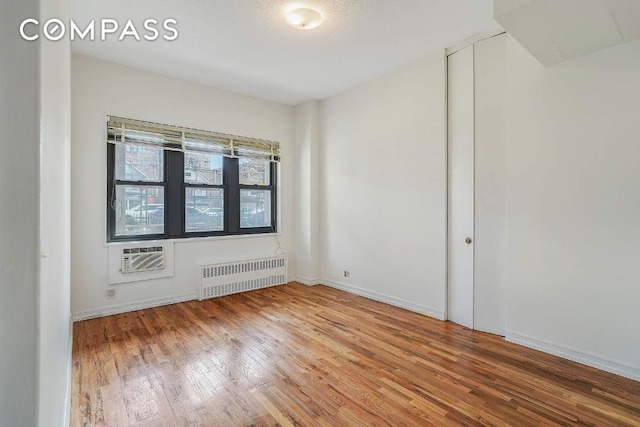 spare room with a wall mounted air conditioner, radiator, and hardwood / wood-style floors