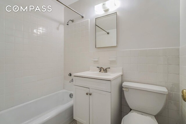 full bathroom with tile walls, tiled shower / bath, vanity, and toilet