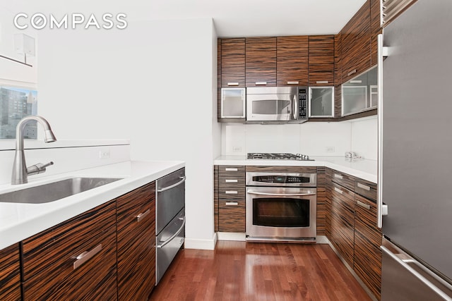 kitchen featuring modern cabinets, dark wood-style flooring, stainless steel appliances, light countertops, and a sink