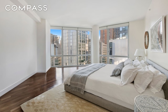 bedroom featuring expansive windows, baseboards, a city view, and wood finished floors