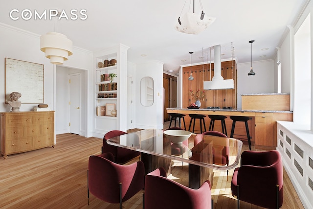 dining room with light wood-type flooring, built in features, and crown molding