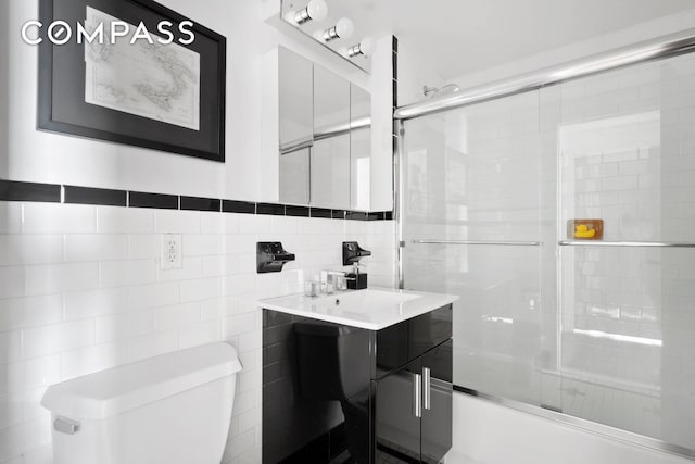 bathroom with tile walls, toilet, vanity, and a shower with shower door