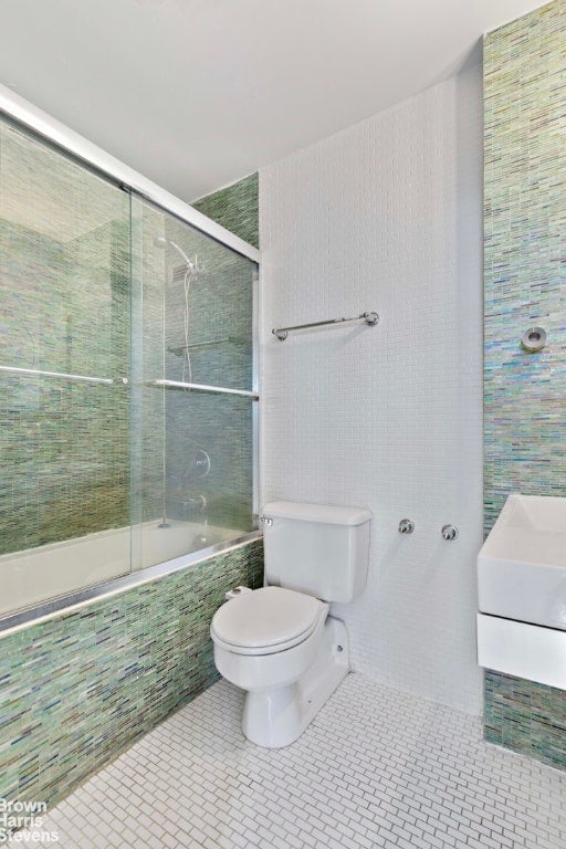 full bathroom featuring tile walls, tile patterned floors, shower / bath combination with glass door, and toilet