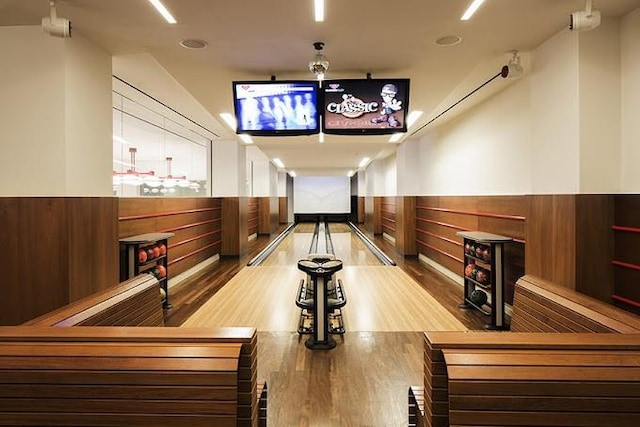 rec room with bowling, wainscoting, wood finished floors, and wood walls