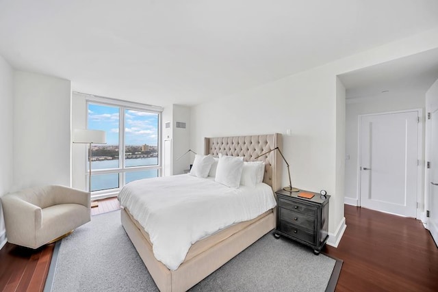 bedroom with wood finished floors, a water view, and baseboards