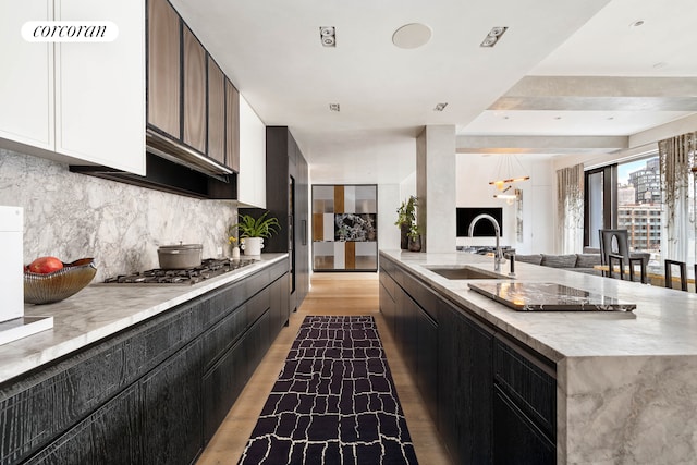 kitchen featuring light stone counters, a sink, light wood-style floors, tasteful backsplash, and stainless steel gas stovetop