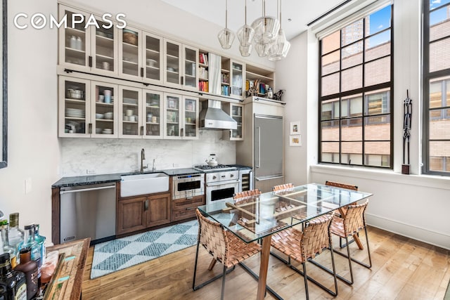 kitchen with stainless steel appliances, wall chimney exhaust hood, a sink, light wood finished floors, and a chandelier