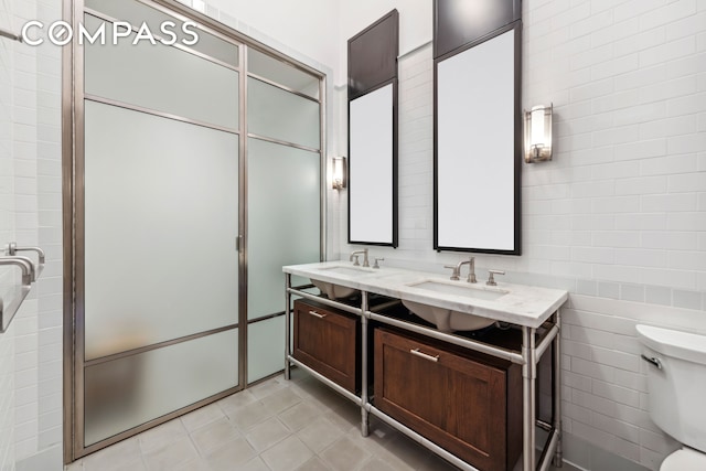 bathroom featuring toilet, double vanity, tile walls, and a sink