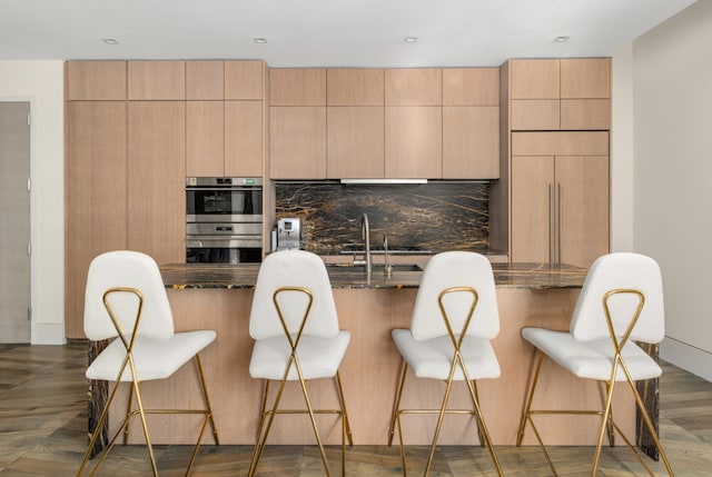 kitchen with light brown cabinetry, sink, dark hardwood / wood-style floors, double oven, and dark stone counters