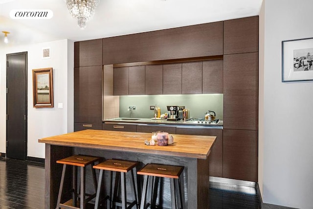 kitchen with dark hardwood / wood-style flooring, a kitchen breakfast bar, dark brown cabinetry, and butcher block counters