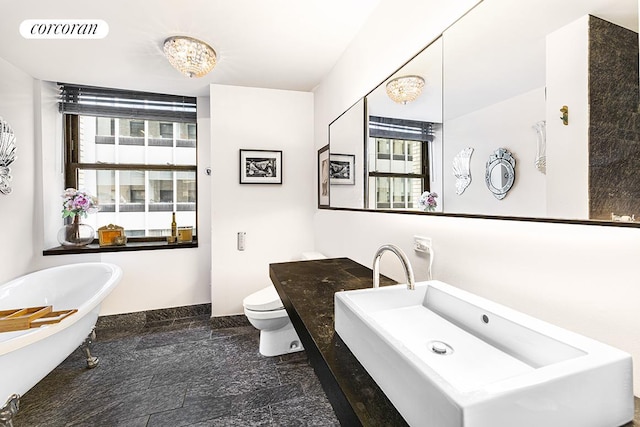 bathroom featuring toilet, vanity, visible vents, a freestanding bath, and baseboards