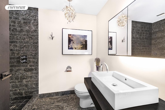 bathroom with tiled shower, toilet, and baseboards