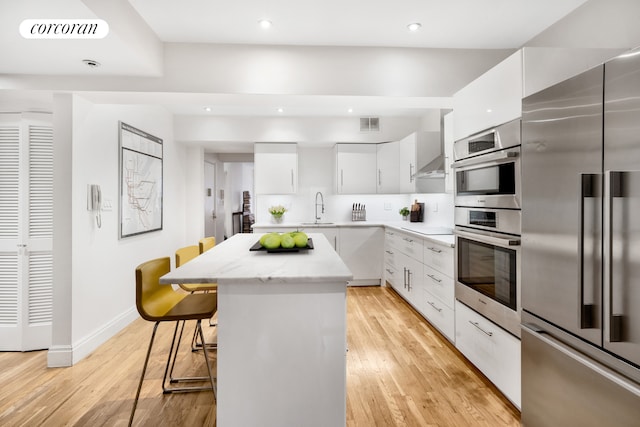 kitchen with visible vents, a kitchen island, a breakfast bar, a sink, and stainless steel appliances