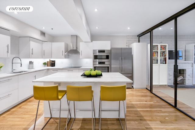 kitchen with stainless steel appliances, visible vents, a sink, and wall chimney exhaust hood