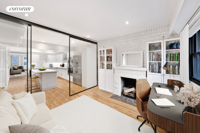 home office with brick wall, light wood-type flooring, visible vents, and a brick fireplace