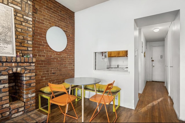 dining space featuring brick wall, baseboards, and dark wood-style flooring